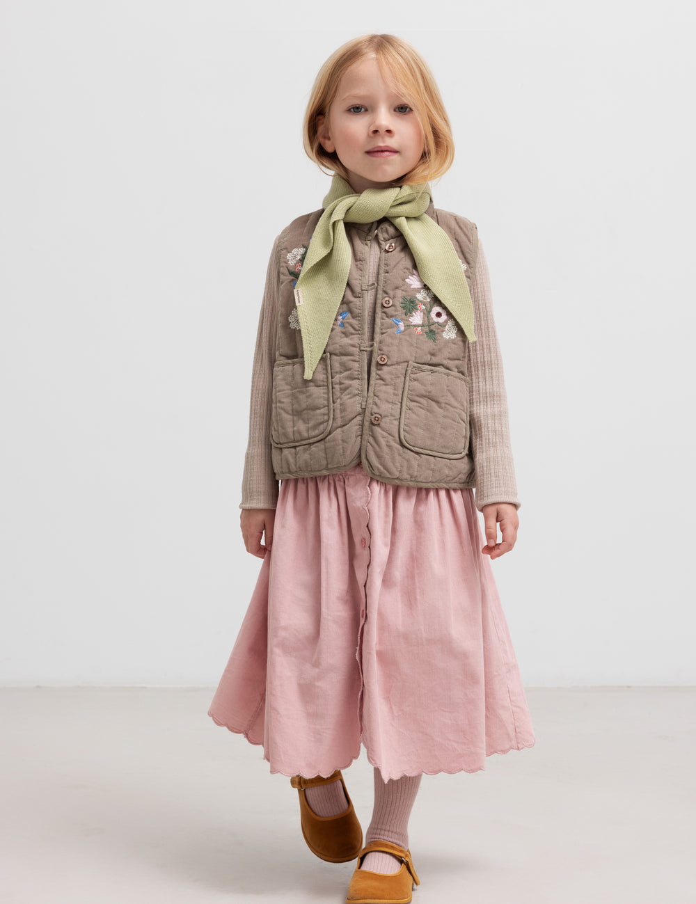Pige iført beige quiltet vest med lommer og lyserød nederdel