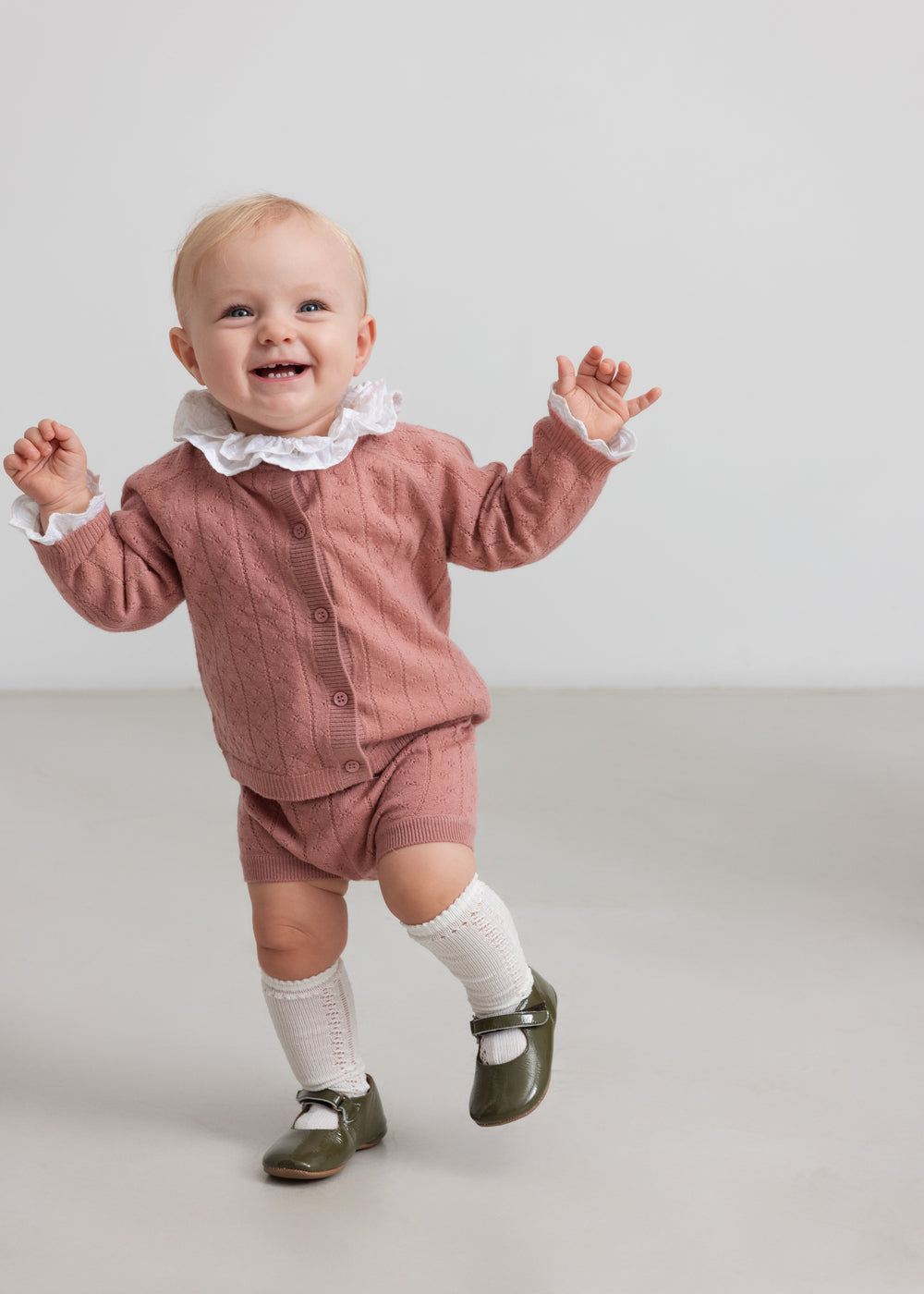 baby iført rosa strikket sæt med hvid flæsekrave