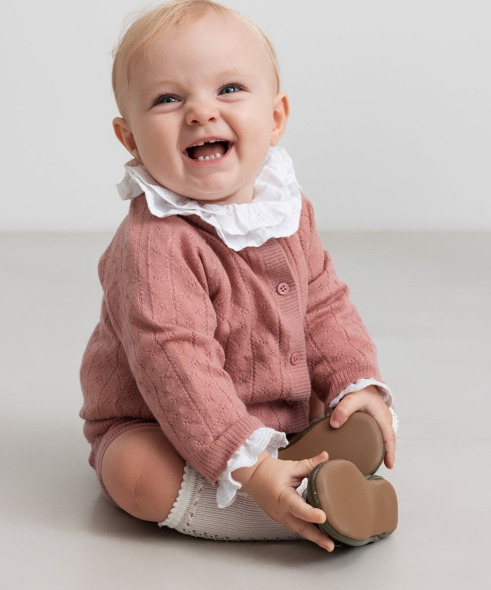 baby iført rosa strikket sæt med hvid flæsekrave
