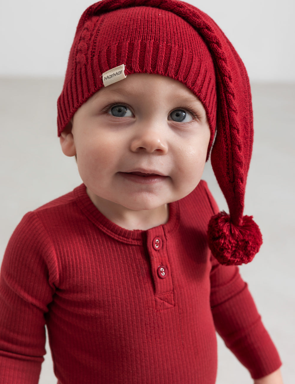 Pige i rød ribstrikket julekjole med flæser på skuldrene og nissehue