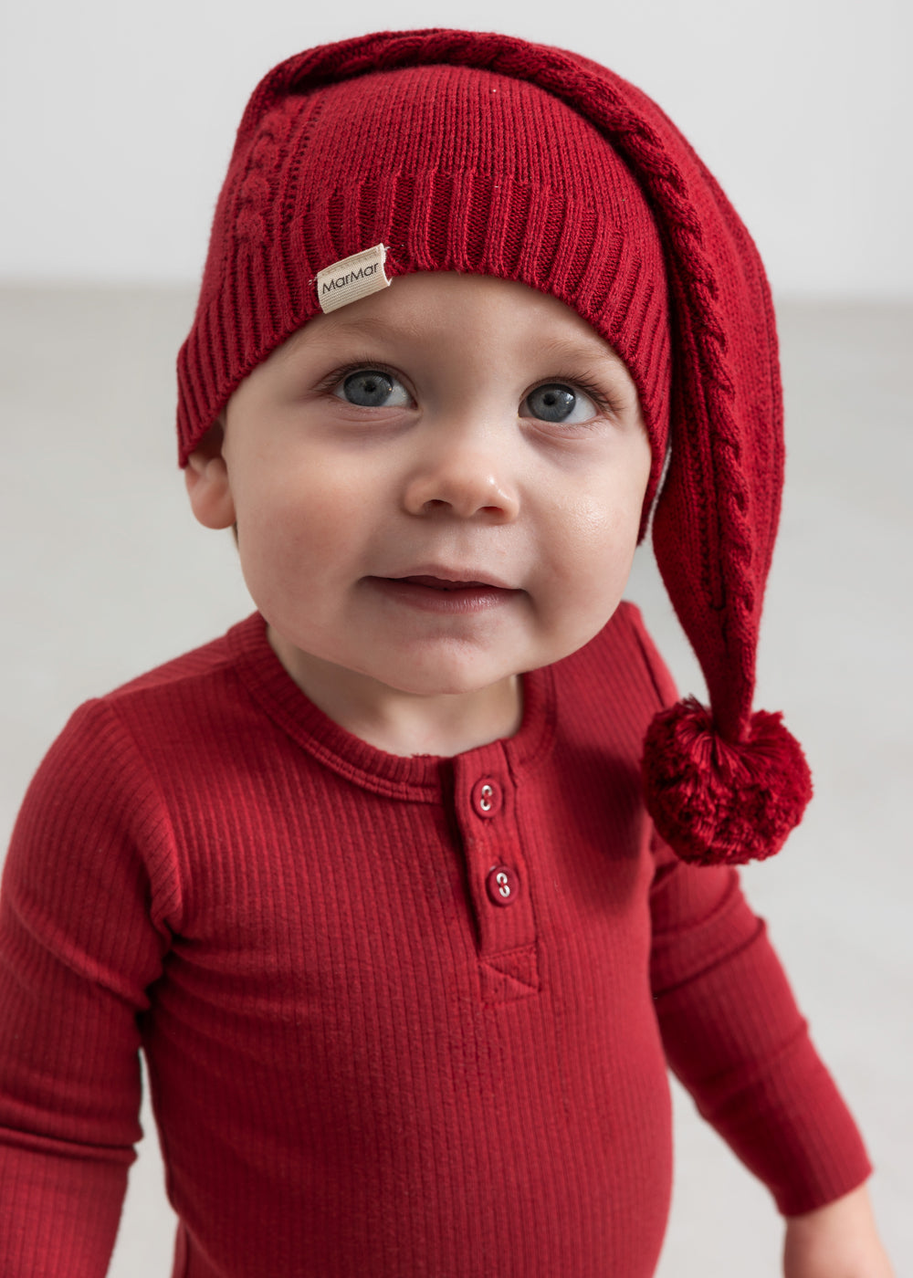 Baby iført rød ribbet body med stolpeknapper og nissehue