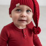 Baby iført rød ribbet body med stolpeknapper og nissehue