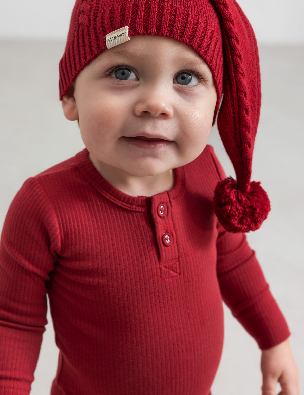 Baby i rød ribbet bluse med knapper og strikket nissehue med kvast