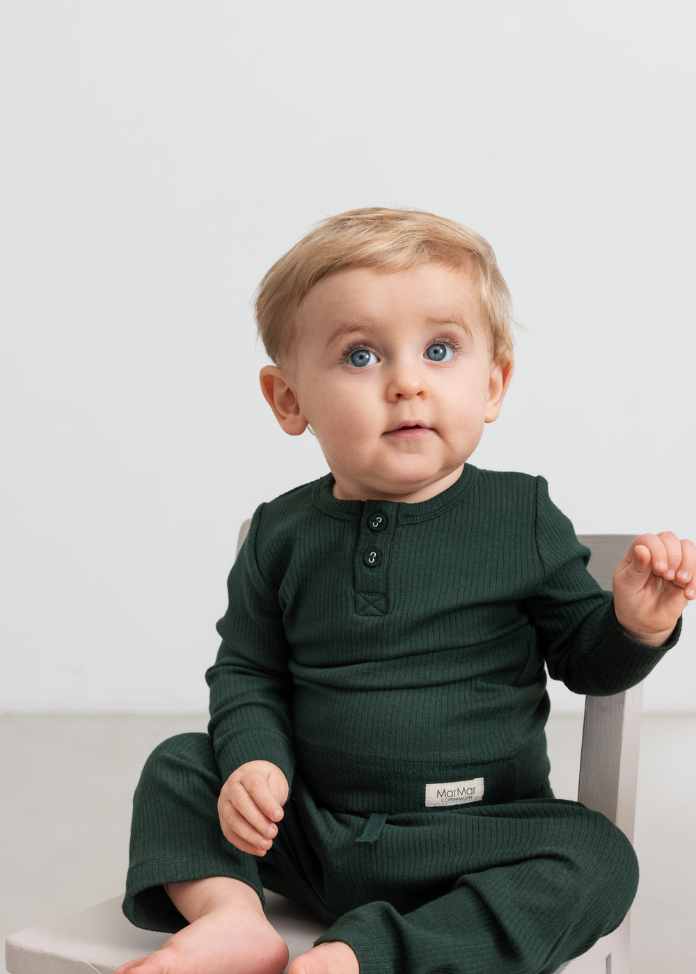 Baby iført mørkegrøn ribbet body med stolpeknapper