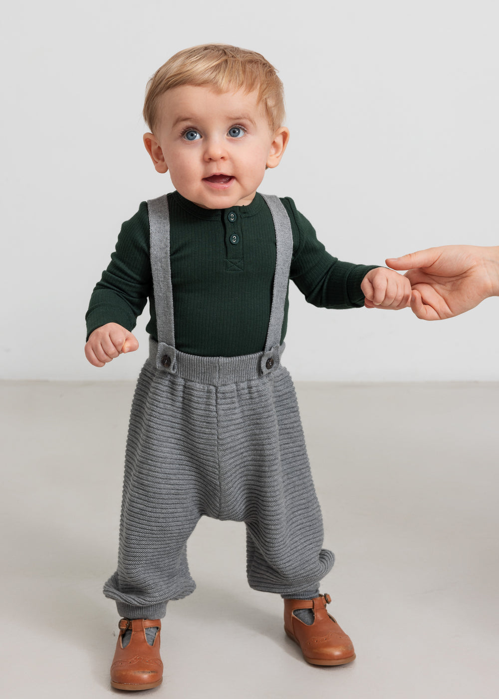 Baby iført mørkegrøn body og grå strikkede bukser med seler