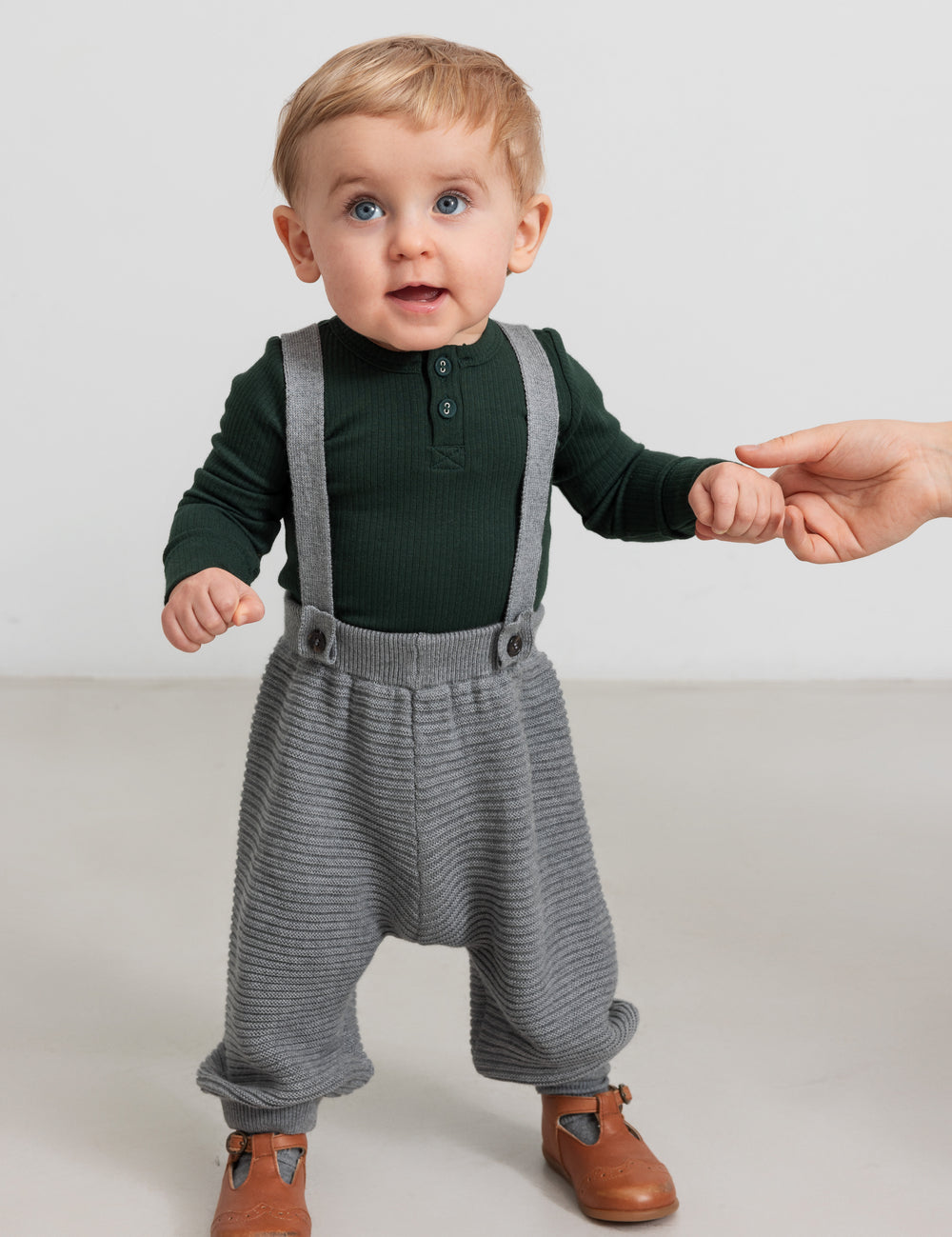 Baby wearing gray knitted suspenders and dark green blouse