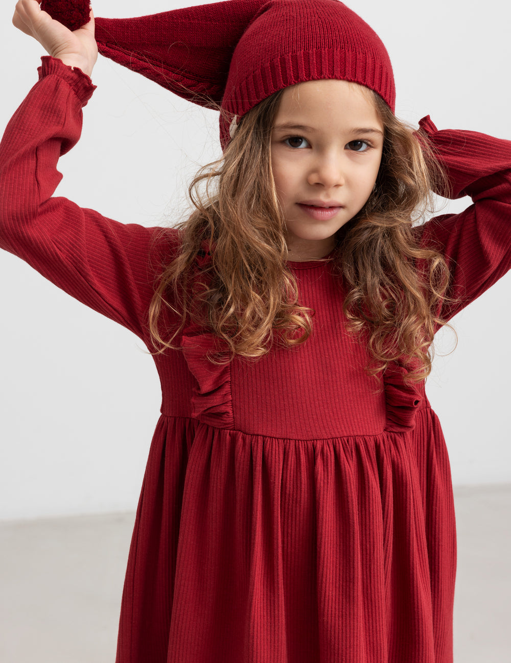 Pige i rød ribstrikket julekjole med flæser på skuldrene og nissehue