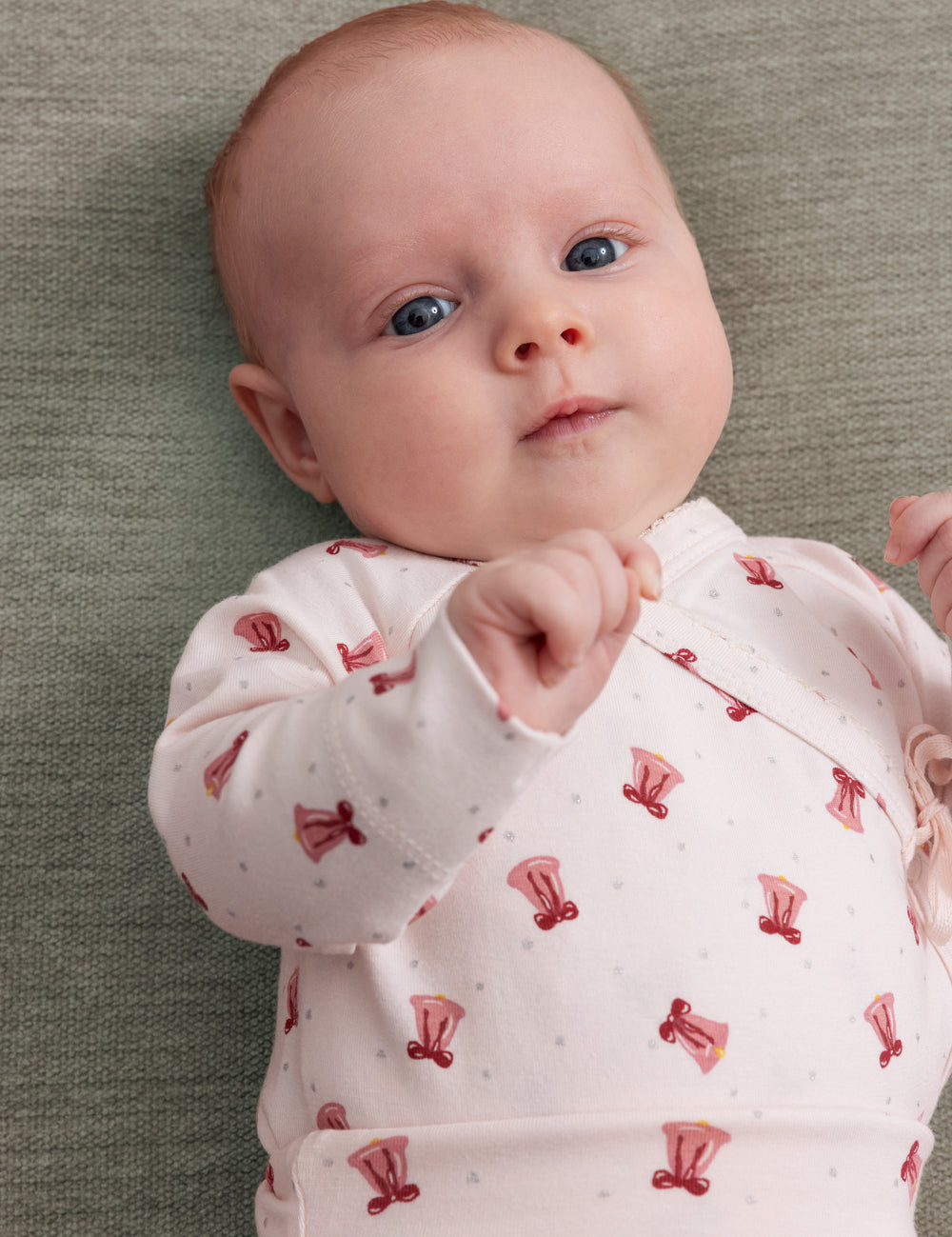 Baby wearing cream-colored wrap top with red Christmas bell print