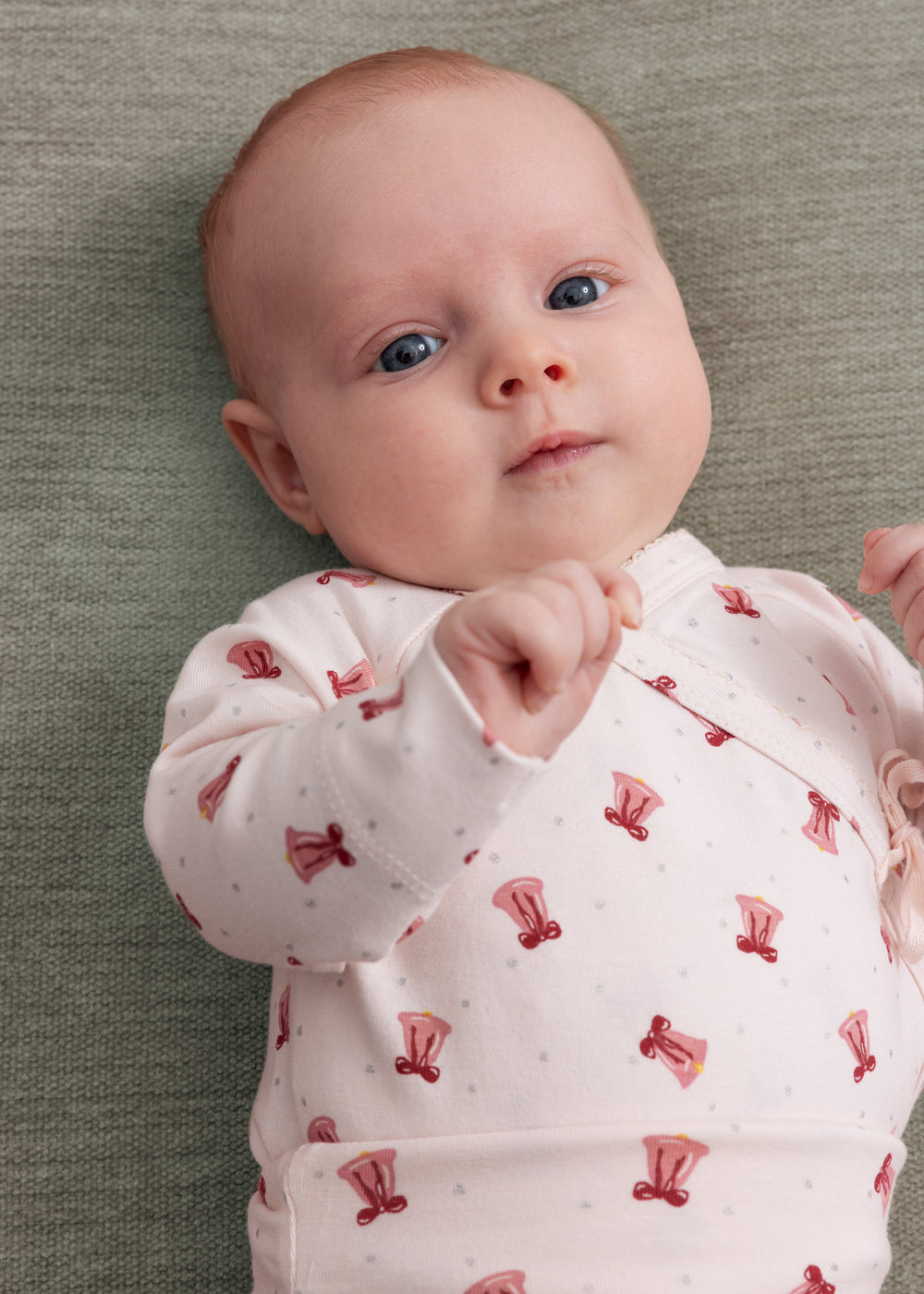 Baby iført cremefarvet slå-om bluse med rødt juleklokkeprint