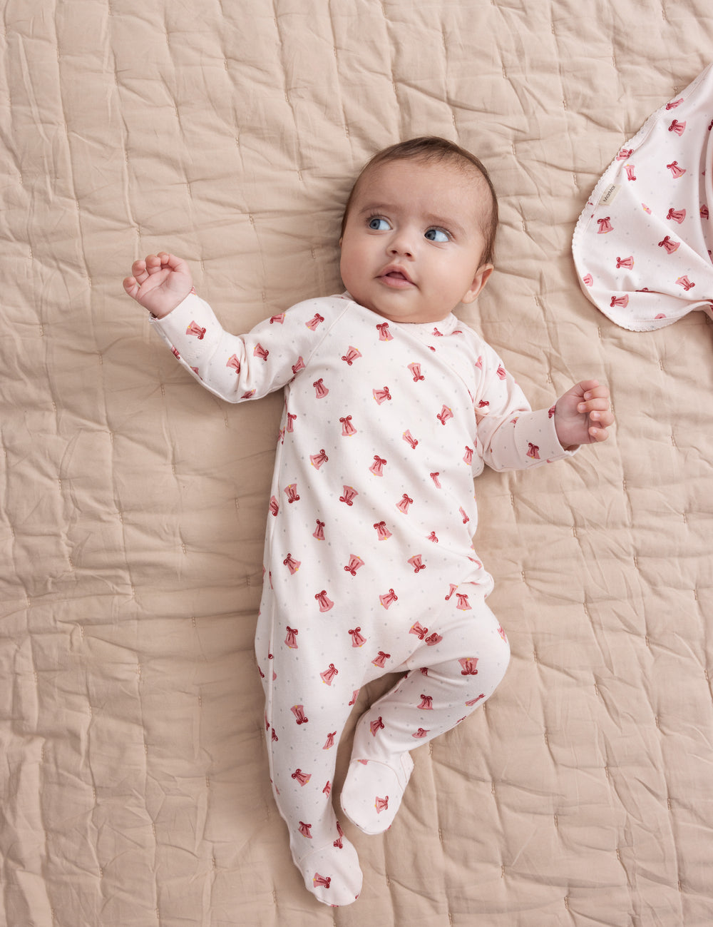 Baby wearing cream-colored onesie with red Christmas bell print lying on blanket