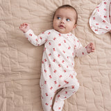 Baby iført cremefarvet heldragt med rødt juleklokkeprint liggende på tæppe