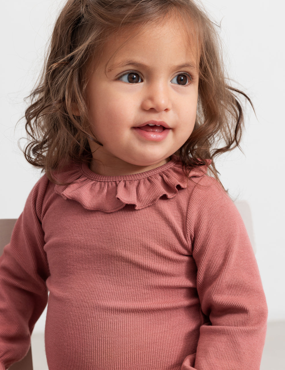 Baby wearing dusty pink bodysuit with ruffle collar