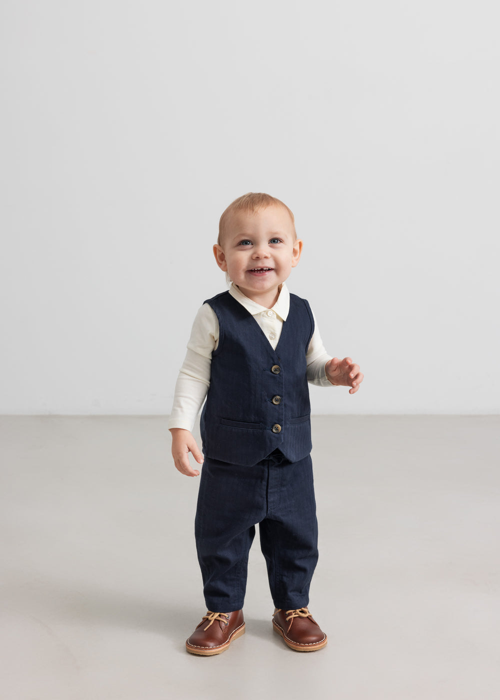 Baby iført mørkeblå vest, skjorte og bukser i festligt julesæt til baby