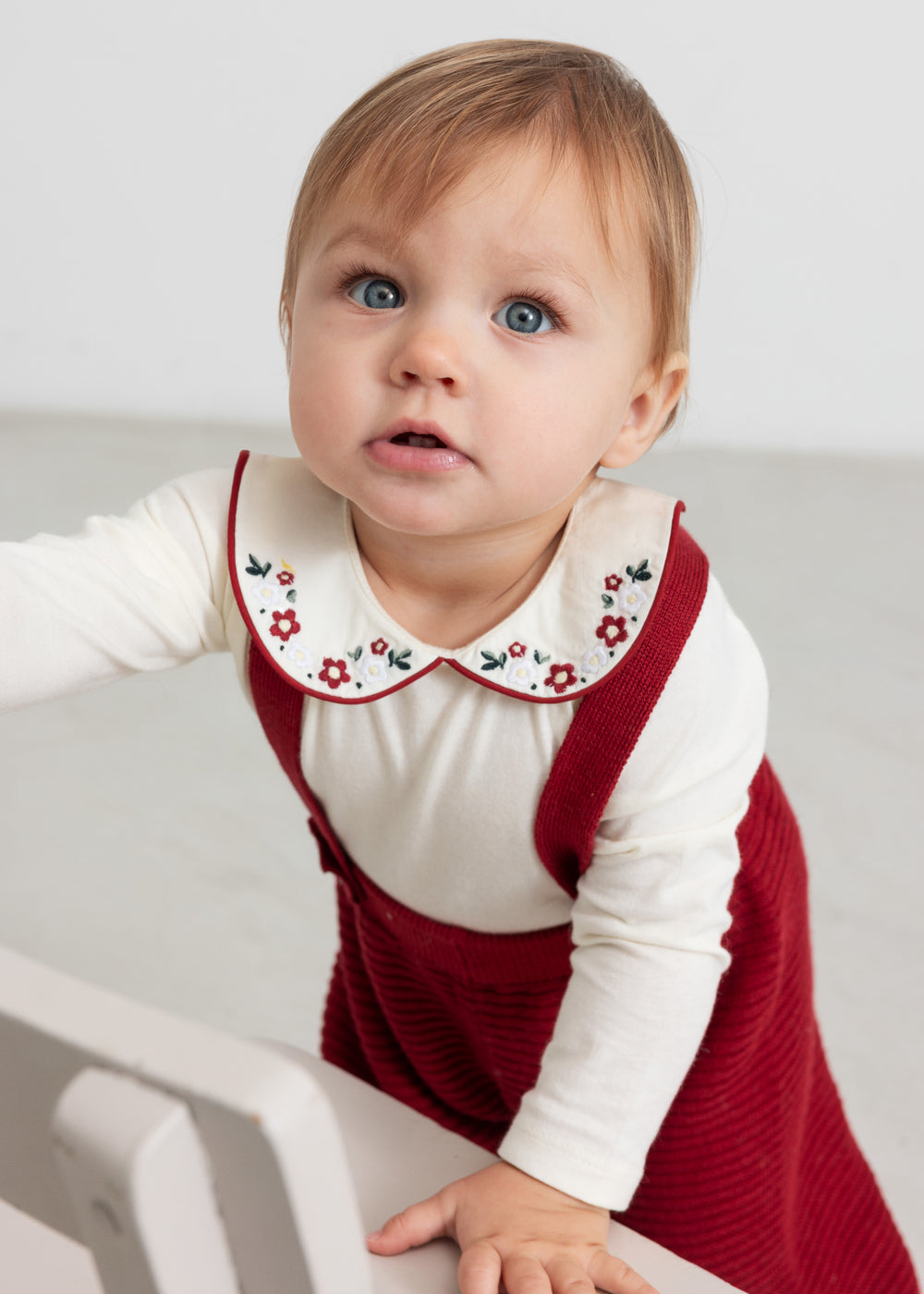 Baby iført hvid bodystocking med blomsterbroderet krave og julerød selekjole