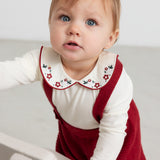 Baby iført hvid bodystocking med blomsterbroderet krave og julerød selekjole