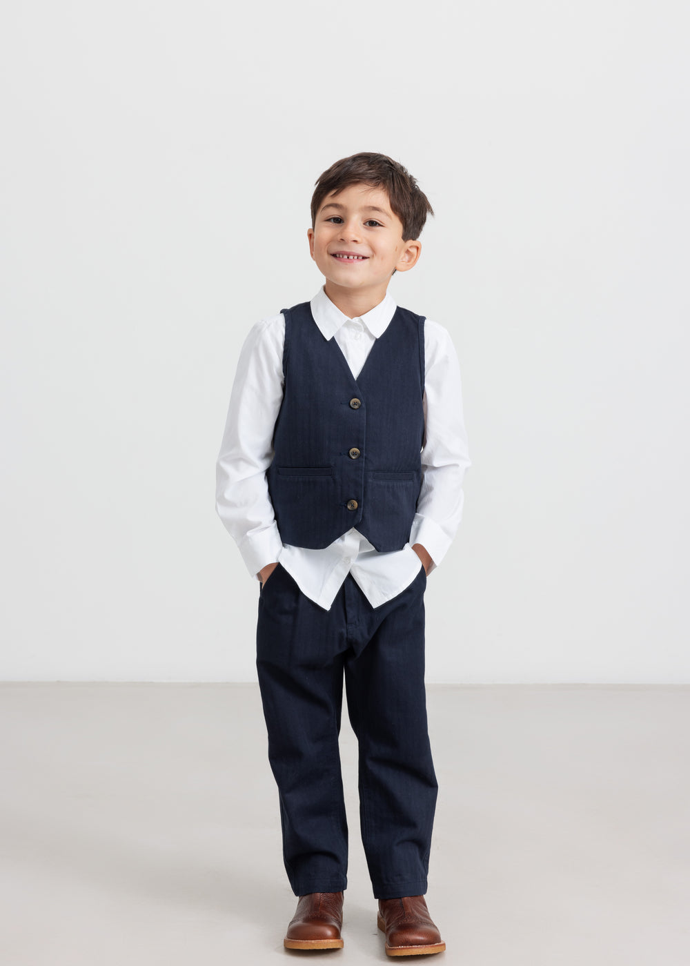 Dreng iført festtøj - mørkeblå bukser, hvid skjorte og vest til børn