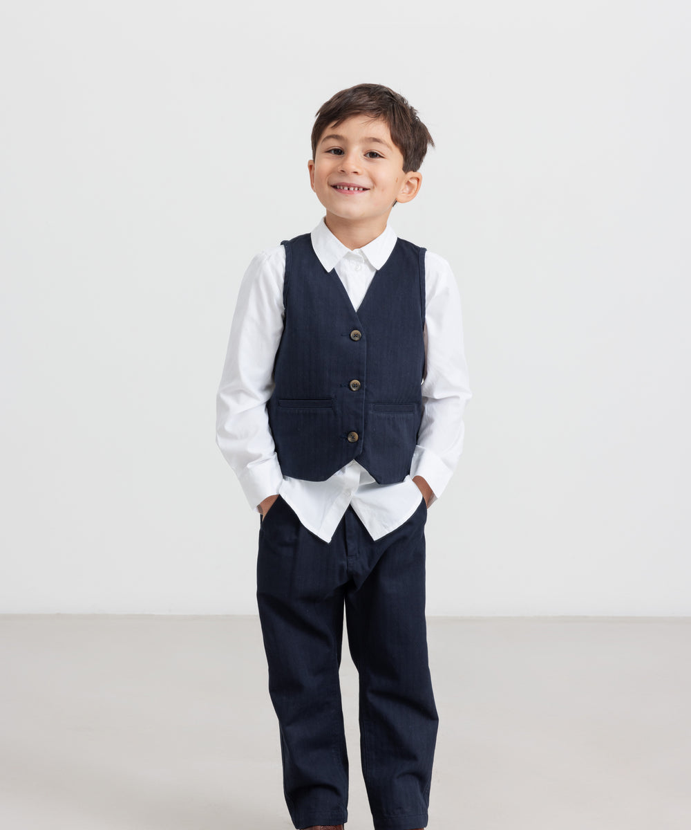 Dreng iført festtøj - mørkeblå bukser, hvid skjorte og vest til børn