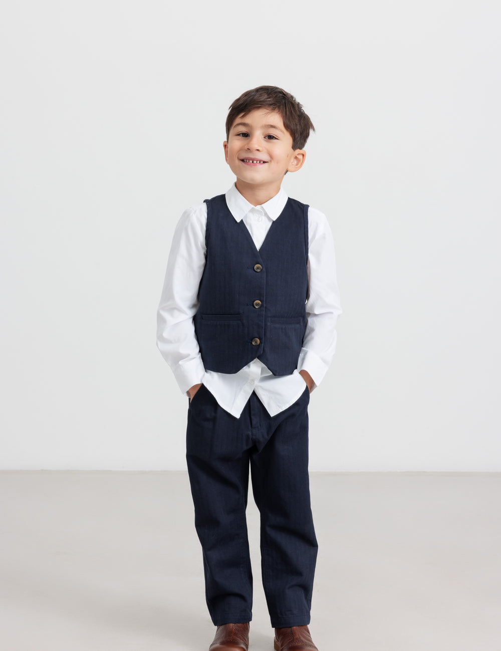 Dreng iført festtøj - mørkeblå bukser, hvid skjorte og vest til børn