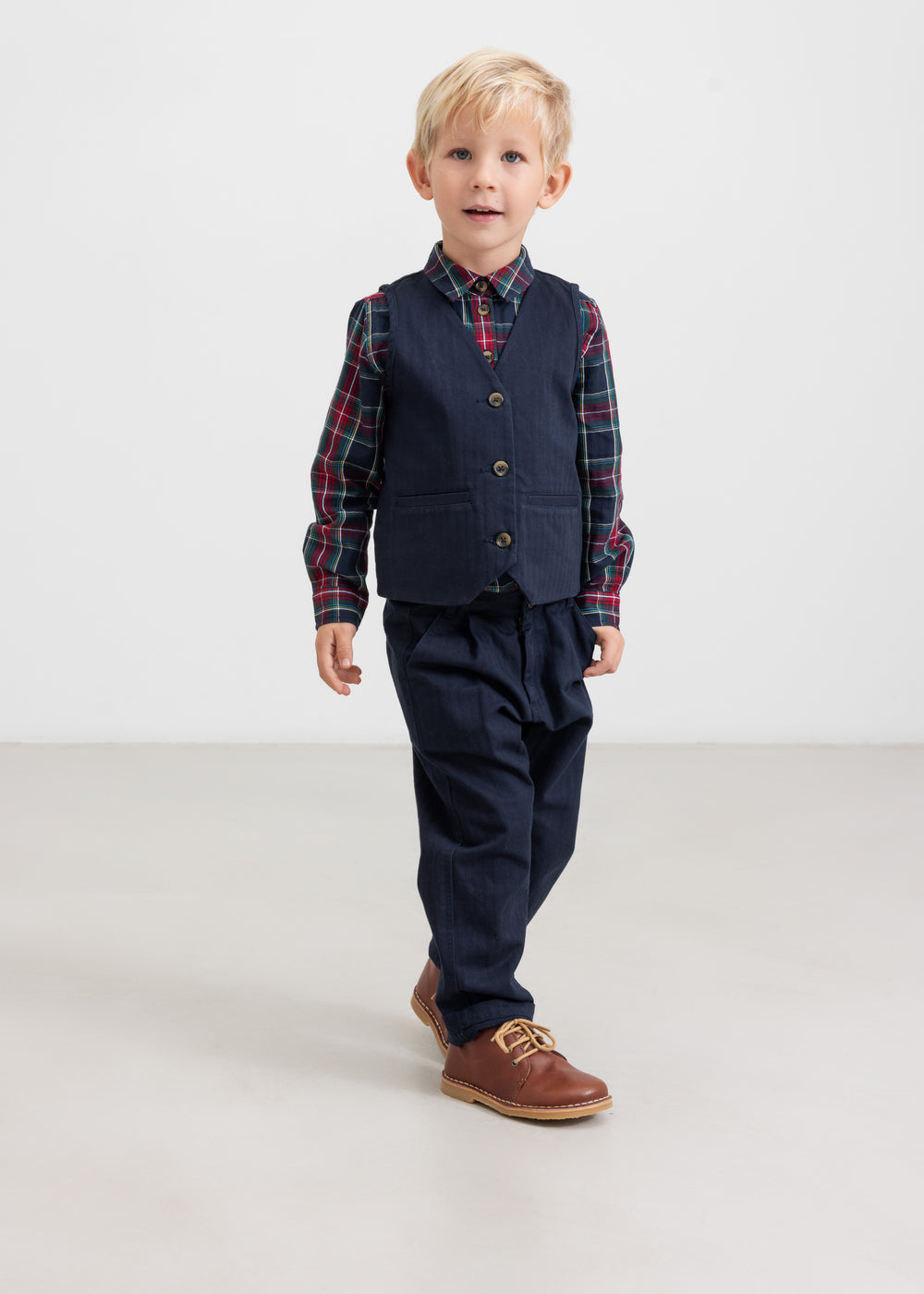 Dreng iført mørkeblå festbukser og vest med ternet skjorte i julelook til børn