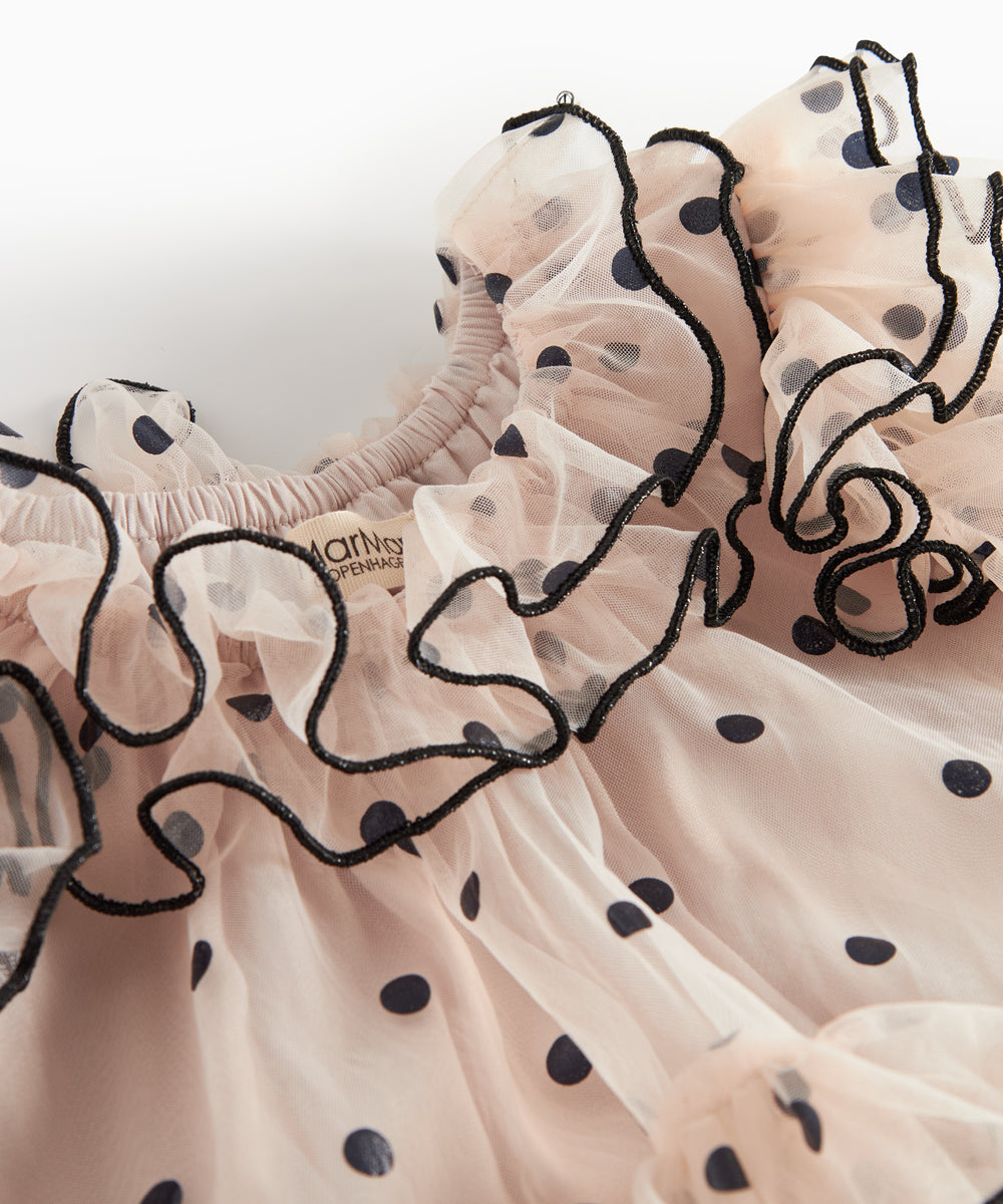 Nærbillede af lyserød tylkjole til børn med sorte prikker og bølgede flæsekanter