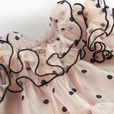 Nærbillede af lyserød tylkjole til børn med sorte prikker og bølgede flæsekanter