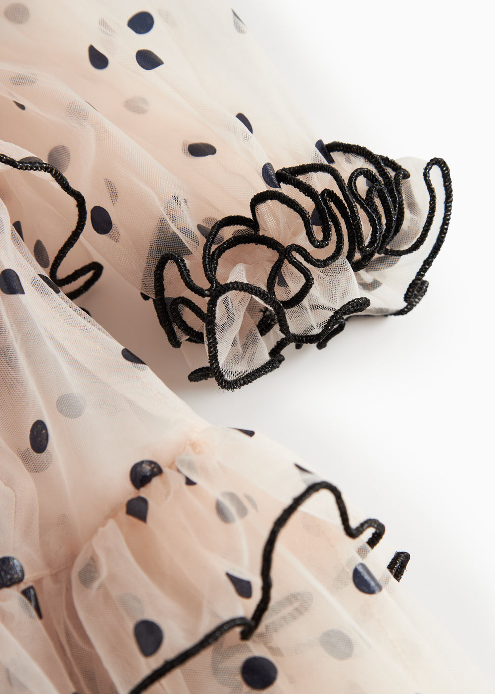 Nærbillede af lyserød tylkjole til børn med sorte prikker og bølgede flæsekanter