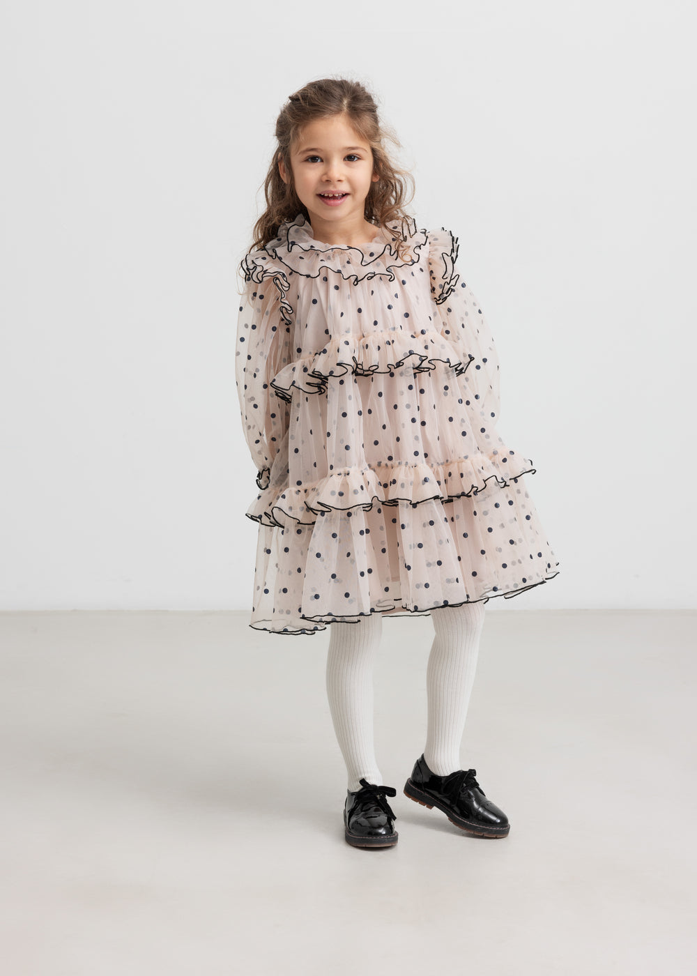 Pige iført lyserød julekjole med dots og cremefarvede strømpebukser til børn
