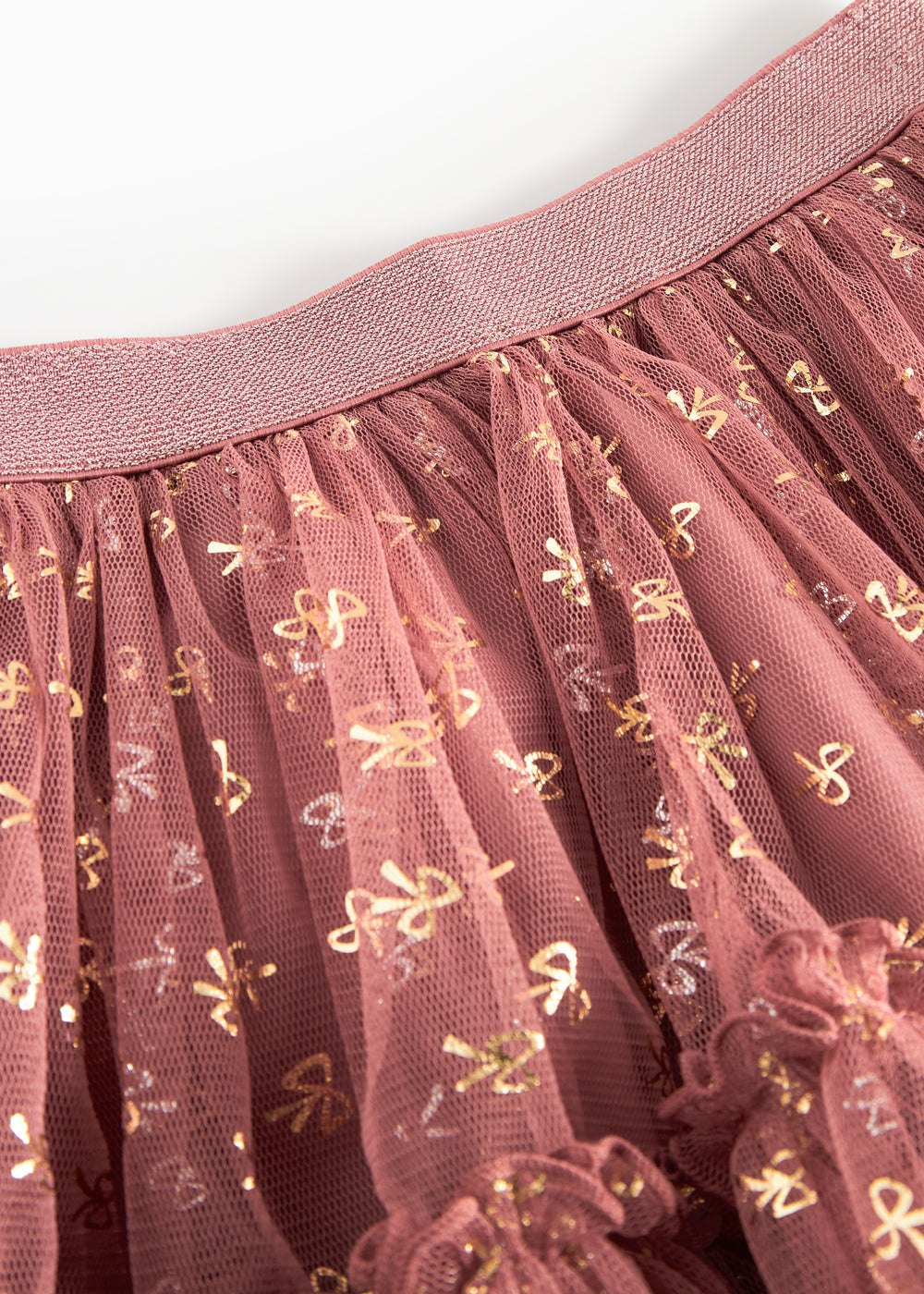 Detalje af tylstof på nederdel til børn med små gyldne prikker og flæser på rosa nederdel