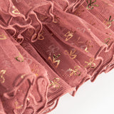 Detalje af tylstof på nederdel til børn med små gyldne prikker og flæser på rosa nederdel