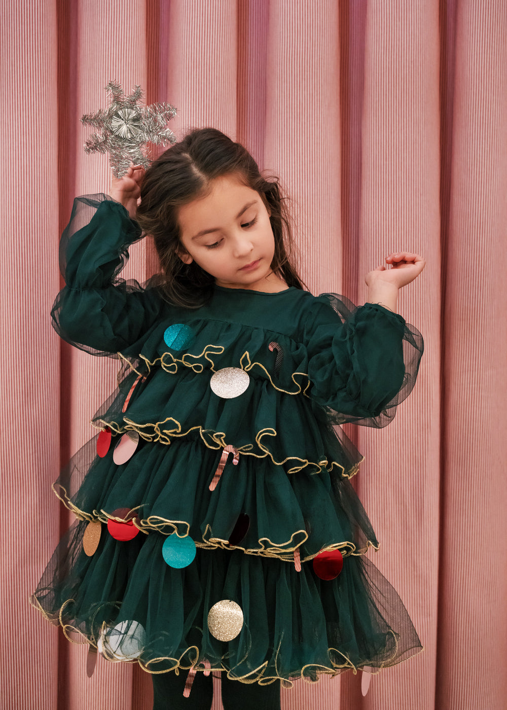 Pige iført mørkegrøn julekjole i tyl med guldkanter og juledetaljer til børn