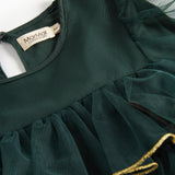 Nærbillede af mørkegrøn julekjole for børn i tyl med guldkanter og flæser