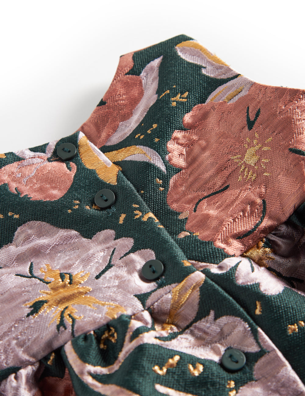 Close-up of dark green shiny fabric with floral print and golden details on baby's party dress