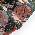 Nærbillede af mørkegrønt glansstof med blomsterprint og gyldne detaljer på festkjole til baby