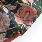Nærbillede af mørkegrønt glansstof med blomsterprint og gyldne detaljer på festkjole til baby