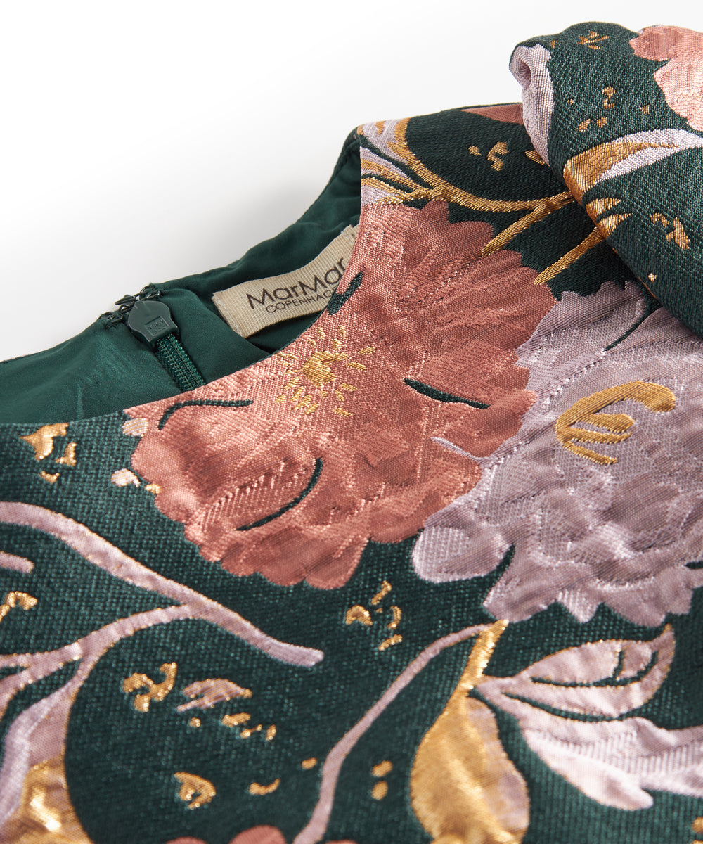 Nærbillede af mørkegrønt glansstof med blomsterprint og gyldne detaljer på festkjole til børn
