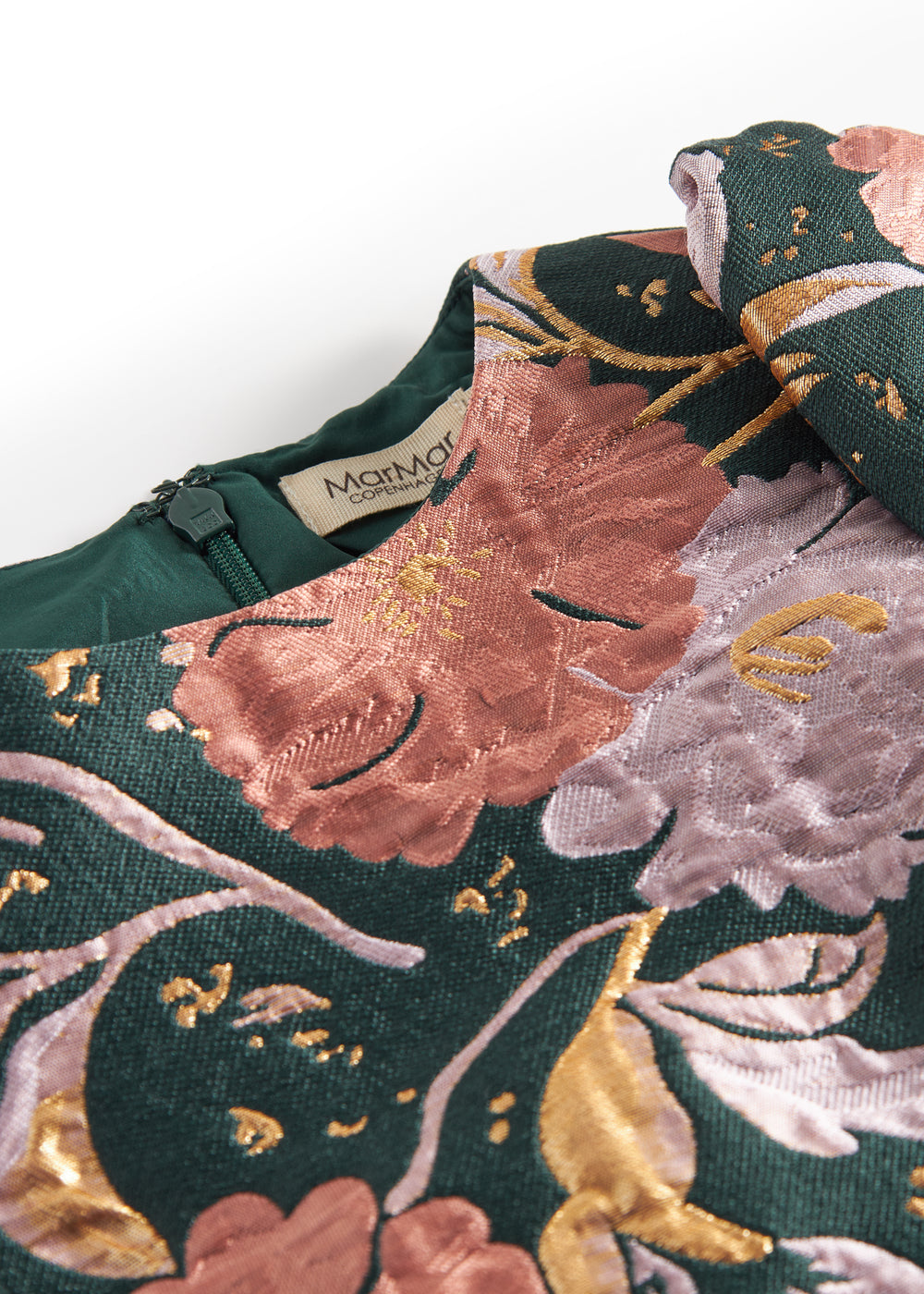 Nærbillede af mørkegrønt glansstof med blomsterprint og gyldne detaljer på festkjole til børn