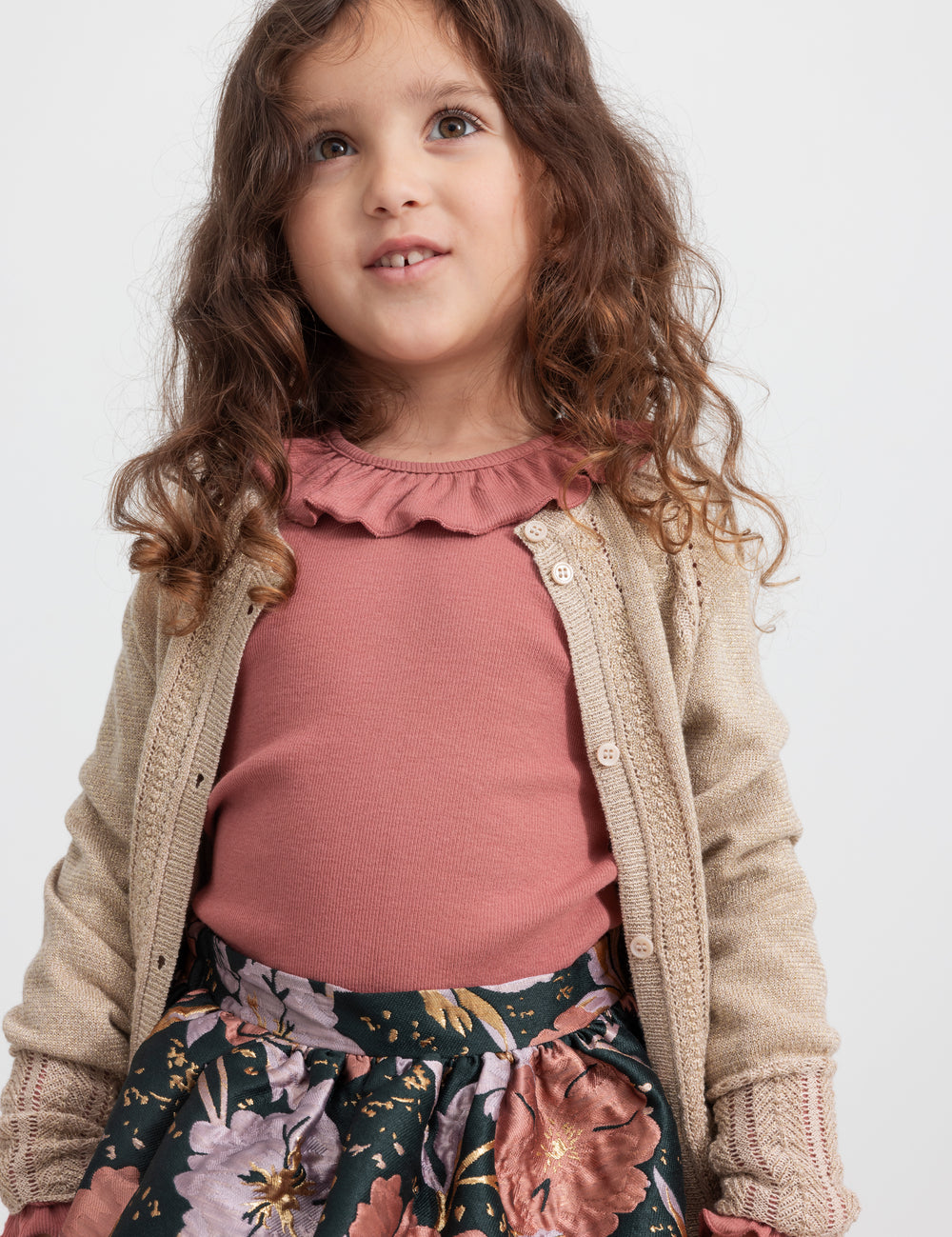 Girl wearing beige cardigan with gold glitter, pink blouse and floral patterned party skirt for children