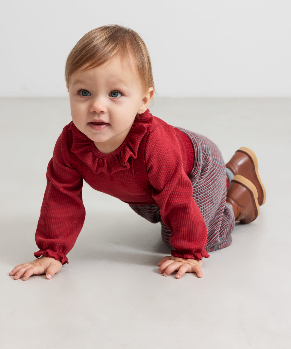 Baby iført strikkede bukser med røde og grå striber og rød juletrøje