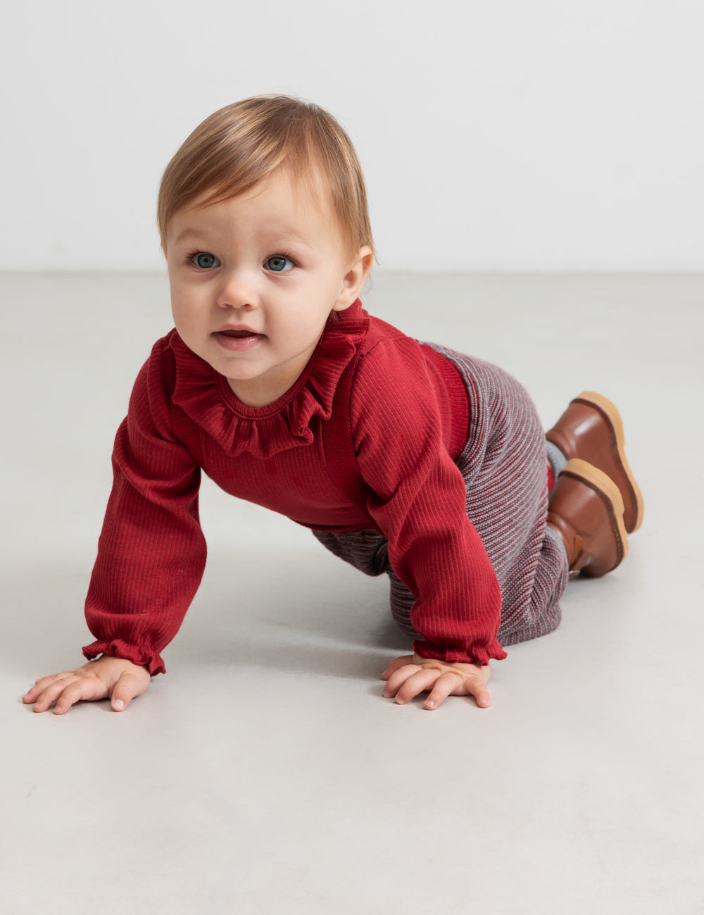 Baby wearing knitted pants with red and gray stripes and red Christmas sweater