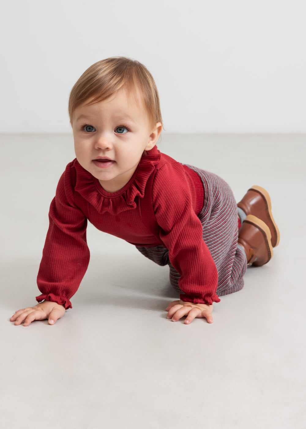 Baby iført strikkede bukser med røde og grå striber og rød juletrøje