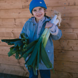 Child wearing a blue knitted hat and blue clothing with carrots in their hands.