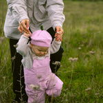 Baby wearing bright red overalls and a matching hat, walking supported by an adult.