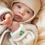 Baby in beige fleece jacket and beige knitted hat set close to