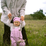 Baby wearing bright red overalls and a matching hat, walking supported by an adult.