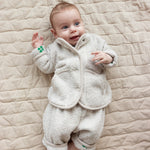 Baby wearing a beige fleece jacket and matching pants lying on a blanket.