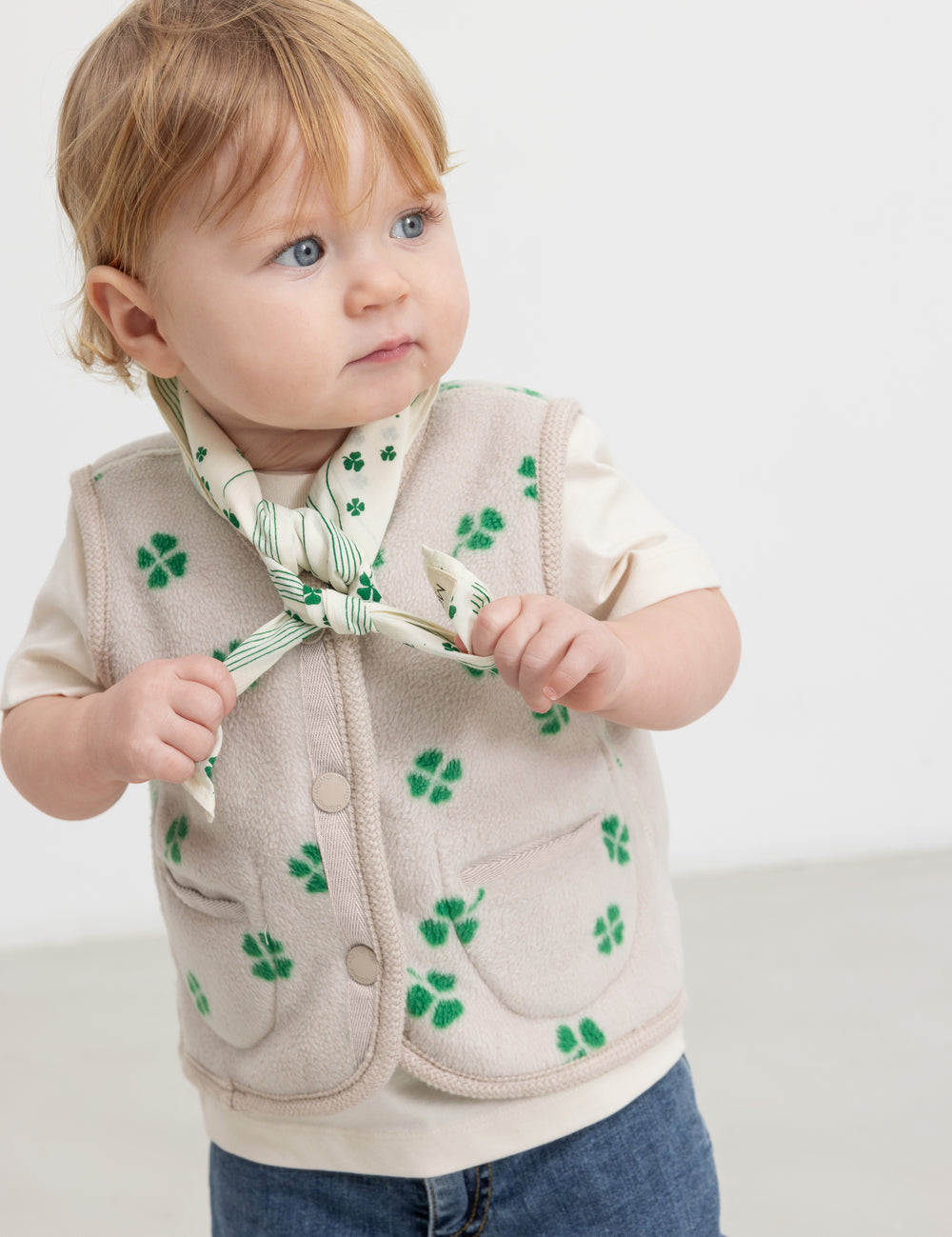Baby wearing a beige bib with a green clover print and matching fleece vest.