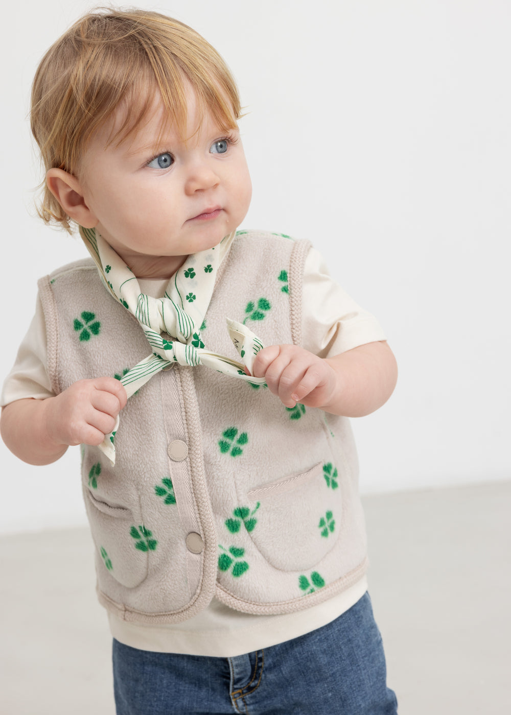 Baby wearing a beige bib with a green clover print and matching fleece vest.