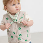 Baby wearing a beige bib with a green clover print and matching fleece vest.