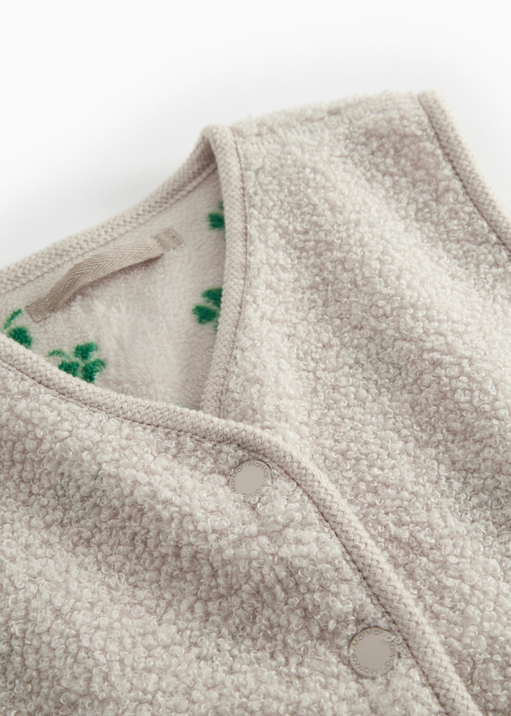 Detalje af beige teddy vest til børn med grønt kløverprint, trykknapper og blød struktur