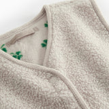 Detalje af beige teddy vest til børn med grønt kløverprint, trykknapper og blød struktur